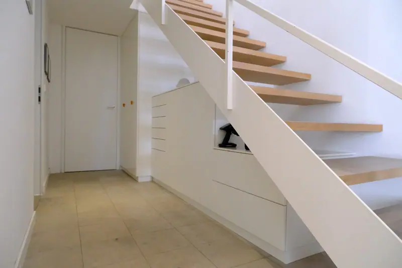 Weißer Einbauschrank mit Auszügen unter einer Treppe mit Eichenstufen